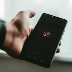 Dłoń trzyma smartfon z logo Instagram. Chcesz wiedzieć, jak zobaczyć relacje na IG?