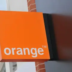 Pomarańczowy szyld Orange z napisem "orange" i symbolem ™. Obok widać fragment okna z napisem "SALE UP TO 70% OFF", sugerujący promocje i kody rabatowe.