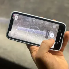 Dłoń trzyma telefon z włączoną aplikacją miarka, która mierzy odległość na powierzchni.