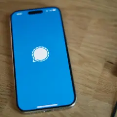 Telefon z niebieskim ekranem i ikoną komunikatora Signal. Obok leży czarny notatnik.