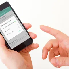 Dłoń trzyma smartfon, na ekranie którego widać ustawienia identyfikatora rozmówcy. Można wybrać "Ukryj numer" lub "Pokazuj numer", gdy dzwoni numer prywatny.