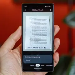 Ręka trzyma smartfon, na ekranie którego działa skaner w telefonie, skanując dokument.