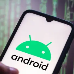 Dłoń trzyma smartfon z logo Android 10. Tło to zielony, rozmyty kod.