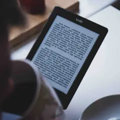 Osoba czyta książkę na czytniku Kindle. Tekst na ekranie jest w formacie epub, a historia opowiada o dżumie w mieście.