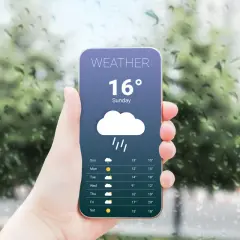 Dłoń trzyma telefon z najlepszą aplikacją pogodową, pokazującą deszczową pogodę i temperaturę 16 stopni.