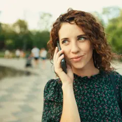 Kobieta z rudymi lokami rozmawia przez telefon, słuchając uważnie. Może właśnie zostawiła wiadomość na poczcie głosowej.