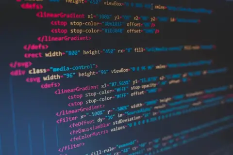 Fragment kodu SVG z definicjami gradientów i filtrów. Widać tagi `<linearGradient>`, `<filter>`, `<feGaussianBlur>`, a także atrybuty takie jak `stop-color` i `width`. To jakby twarda spacja w kodzie, która porządkuje strukturę.