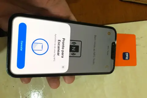iPhone gotowy do skanowania tagu NFC. Obok telefonu leży pomarańczowa karta z logo banku.