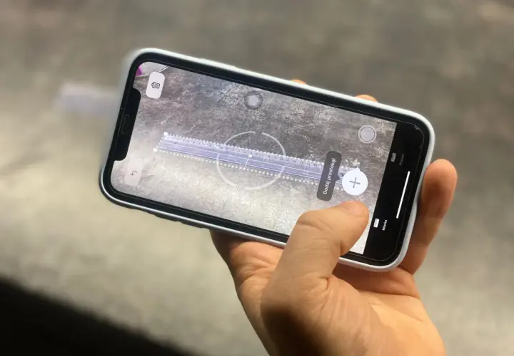 Dłoń trzyma telefon z włączoną aplikacją miarka, która mierzy odległość na powierzchni.
