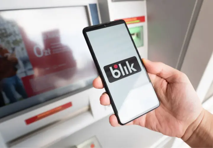 Dłoń trzyma smartfon z logo Blik. Czy Blik jest tylko w Polsce? Płatność zbliżeniowa przy bankomacie.