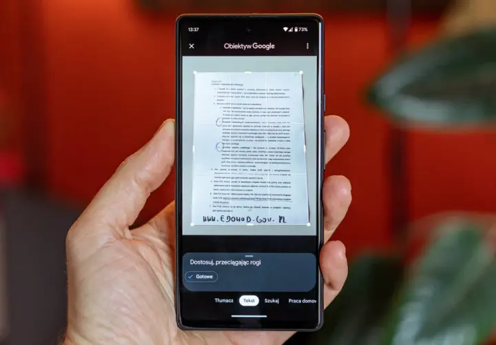 Ręka trzyma smartfon, na ekranie którego działa skaner w telefonie, skanując dokument.