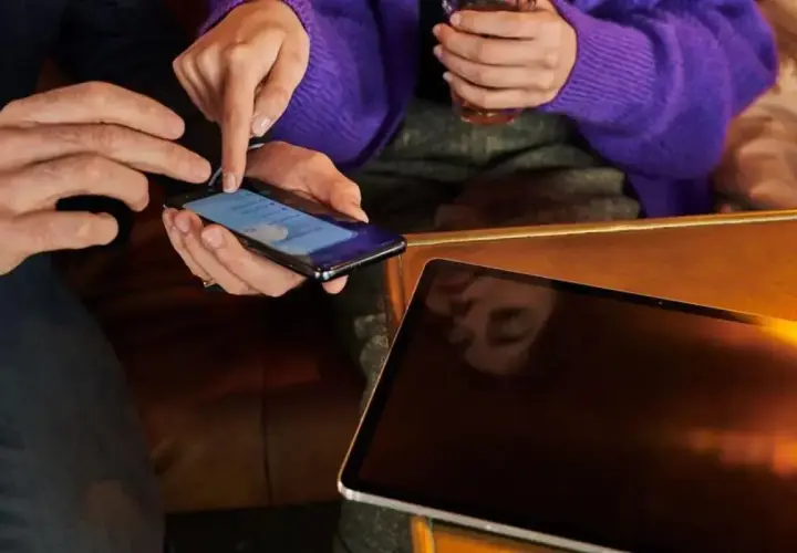 Dłonie pokazują, jak zwiększyć litery w telefonie. Obok leży tablet.