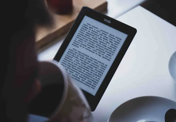 Osoba czyta książkę na czytniku Kindle. Tekst na ekranie jest w formacie epub, a historia opowiada o dżumie w mieście.