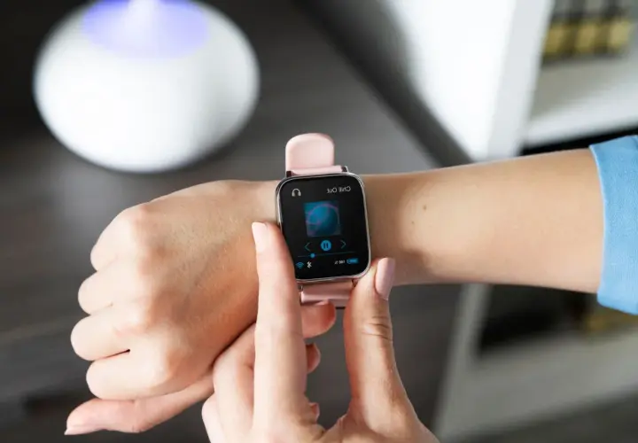 Różowy smartwatch na nadgarstku pokazuje ekran odtwarzania muzyki. Dowiedz się, jak sparować zegarek z telefonem, by cieszyć się ulubionymi utworami.