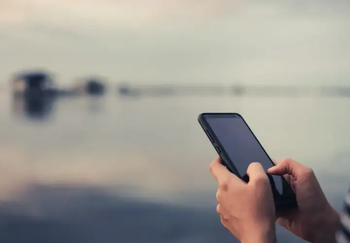 Dłonie trzymające smartfon na tle rozmytego krajobrazu.