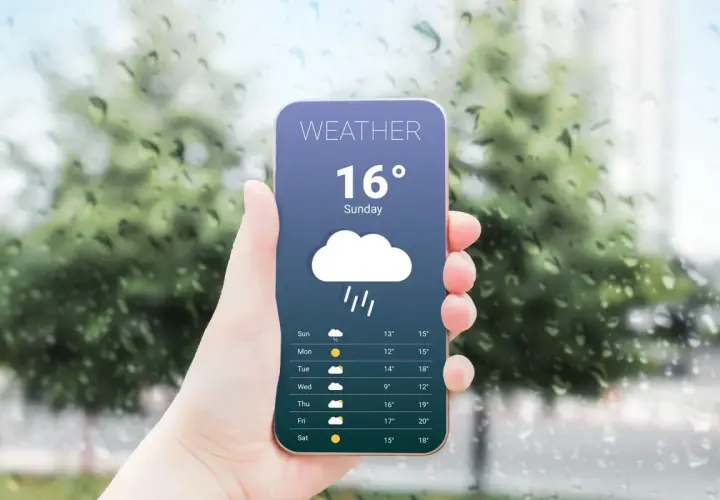 Dłoń trzyma telefon z najlepszą aplikacją pogodową, pokazującą deszczową pogodę i temperaturę 16 stopni.