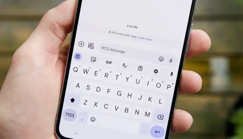 Dłoń trzyma smartfon z włączoną klawiaturą. Na ekranie widoczny jest czat RCS z Judy.