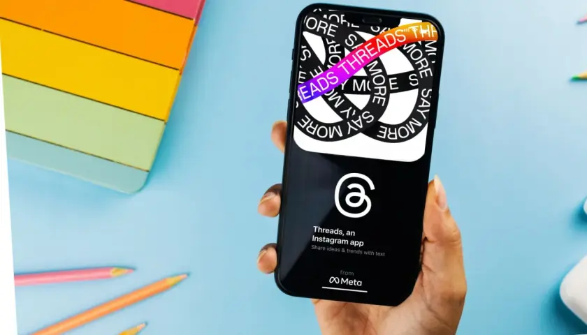 Dłoń trzyma smartfon z aplikacją Threads. Na ekranie widać hasła "Say More" i "Threads", co wyjaśnia, threads co to za aplikacja.