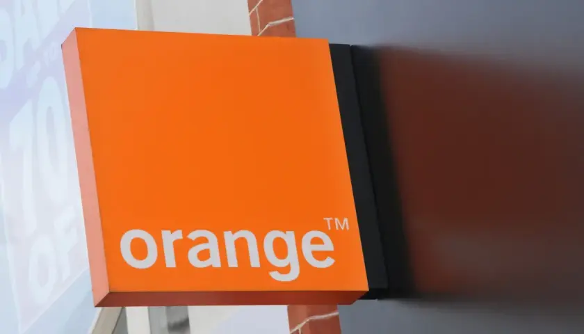 Pomarańczowy szyld Orange z napisem "orange" i symbolem ™. Obok widać fragment okna z napisem "SALE UP TO 70% OFF", sugerujący promocje i kody rabatowe.