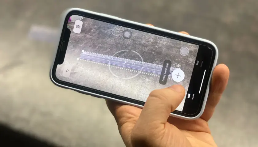Dłoń trzyma telefon z włączoną aplikacją miarka, która mierzy odległość na powierzchni.