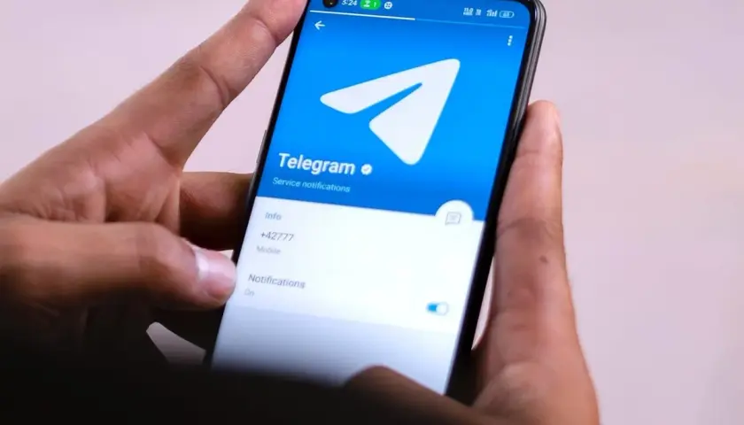 Dłonie trzymają smartfon z otwartą aplikacją Telegram. Widać logo i opcje powiadomień, idealne do dyskretnych rozmów w tajnych grupach Telegram.