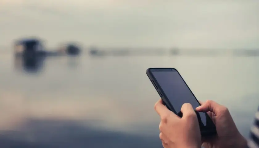 Dłonie trzymające smartfon na tle rozmytego krajobrazu.