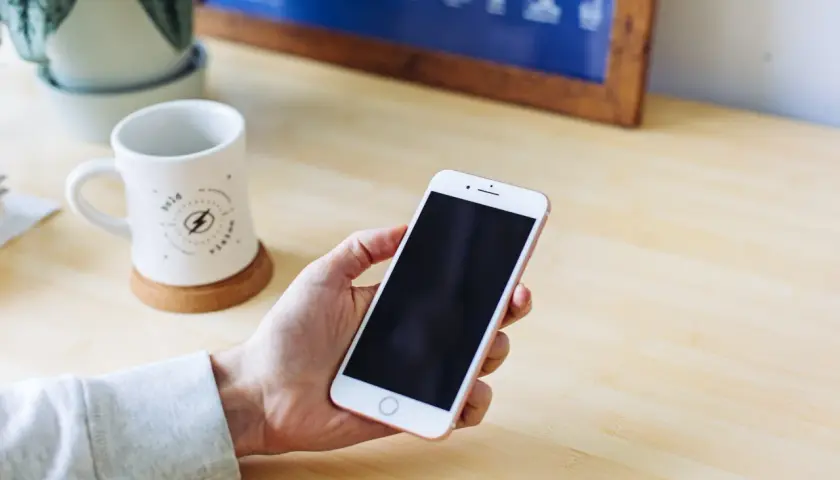 Dłoń trzyma smartfon, na którym widać pusty schowek w telefonie. Obok stoi kubek i roślina.