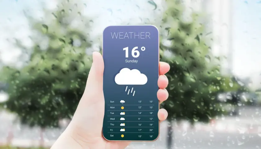 Dłoń trzyma telefon z najlepszą aplikacją pogodową, pokazującą deszczową pogodę i temperaturę 16 stopni.