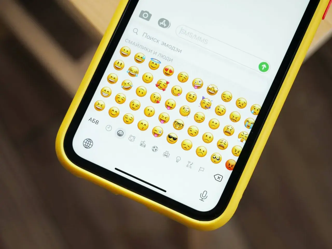 Na ekranie telefonu w żółtej obudowie widać klawiaturę z mnóstwem wesołych i smutnych emotek.