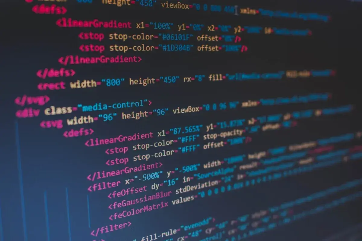 Fragment kodu SVG z definicjami gradientów i filtrów. Widać tagi `<linearGradient>`, `<filter>`, `<feGaussianBlur>`, a także atrybuty takie jak `stop-color` i `width`. To jakby twarda spacja w kodzie, która porządkuje strukturę.