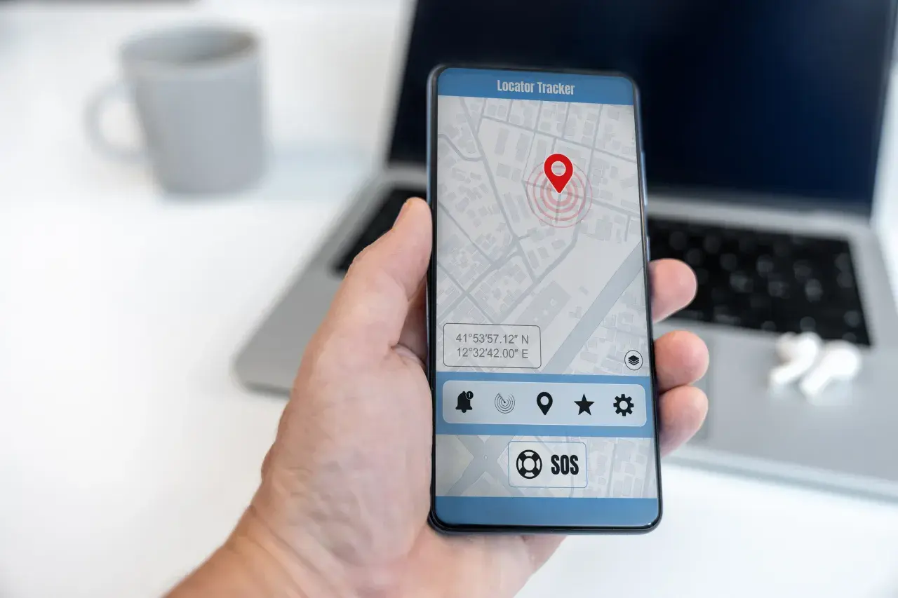 Dłoń trzyma smartfon z mapą i pinezką lokalizatora. To najlepsza darmowa aplikacja do śledzenia telefonu, z przyciskiem SOS.