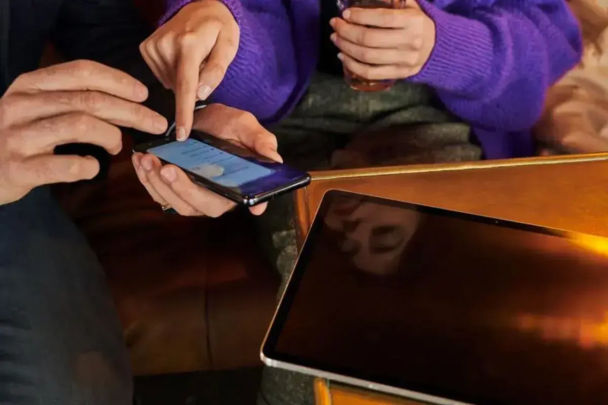 Dłonie pokazują, jak zwiększyć litery w telefonie. Obok leży tablet.