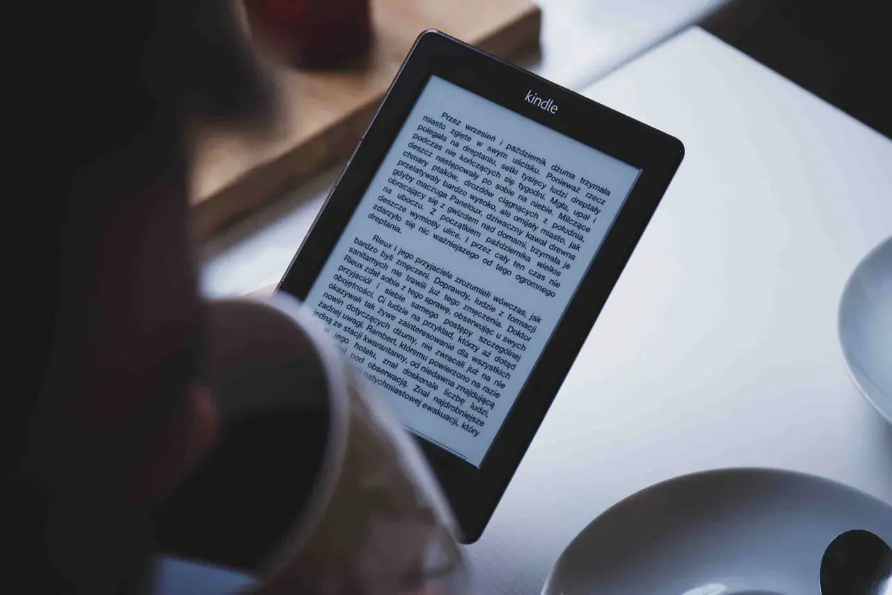 Osoba czyta książkę na czytniku Kindle. Tekst na ekranie jest w formacie epub, a historia opowiada o dżumie w mieście.