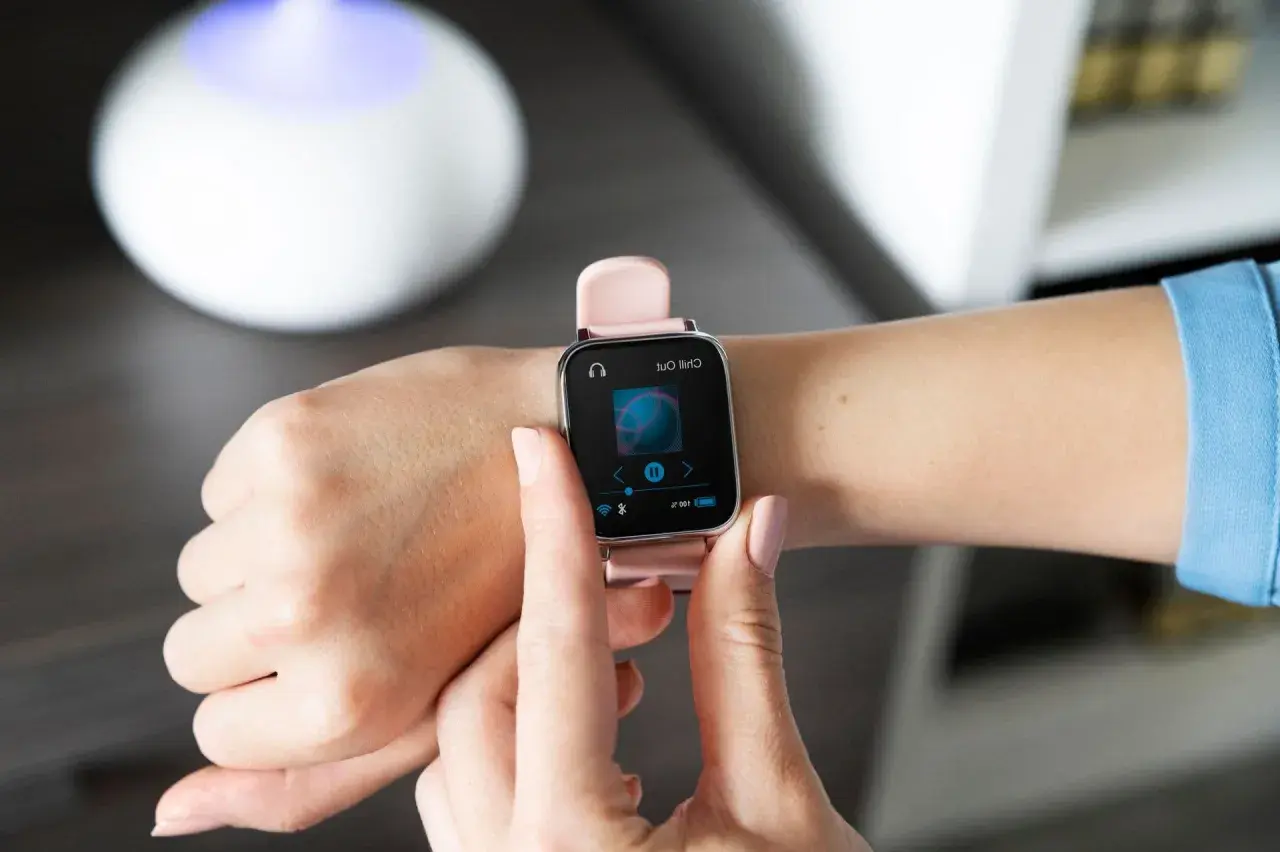 Różowy smartwatch na nadgarstku pokazuje ekran odtwarzania muzyki. Dowiedz się, jak sparować zegarek z telefonem, by cieszyć się ulubionymi utworami.