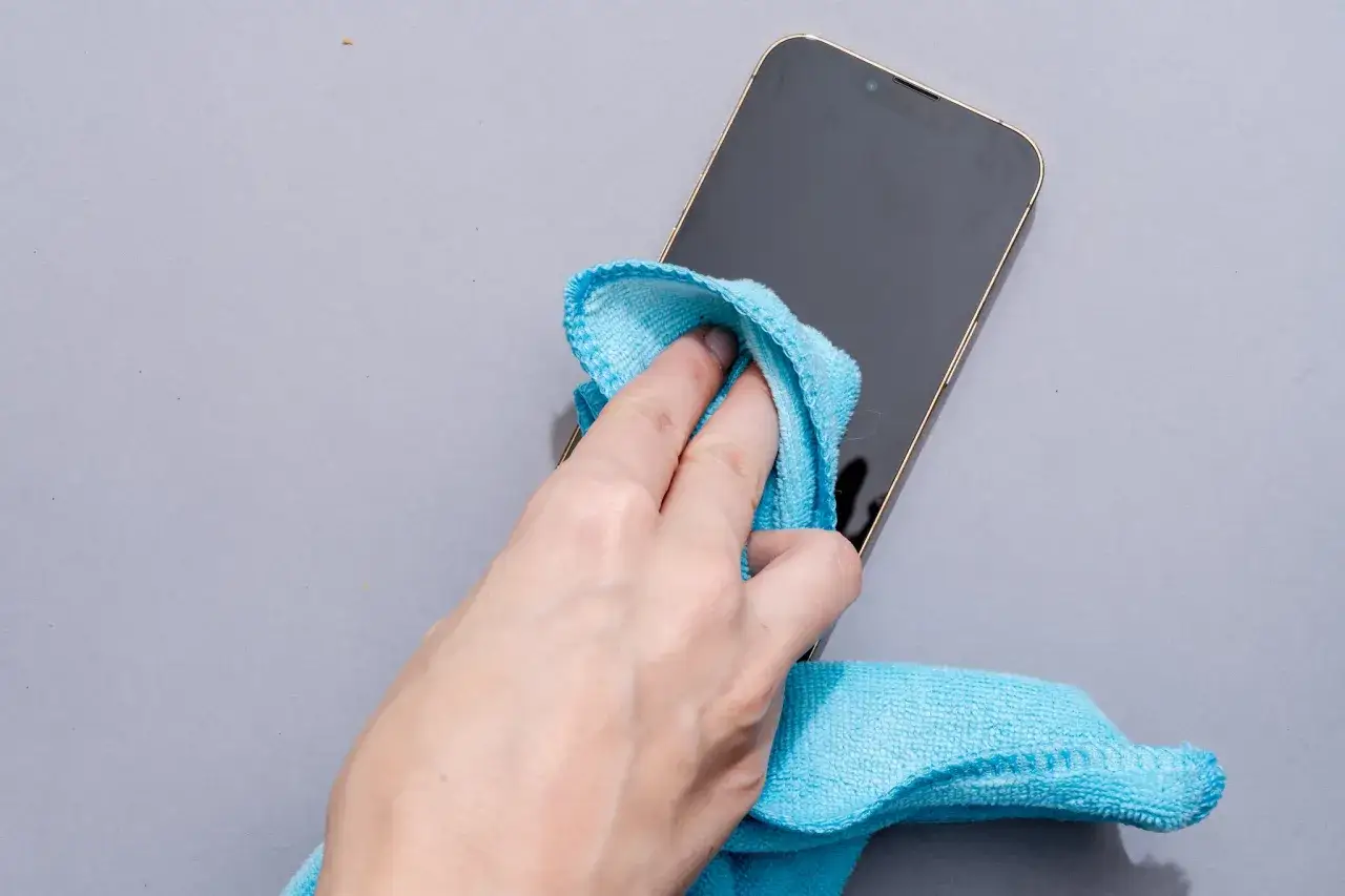 Dłoń z niebieską ściereczką czyści ekran telefonu.