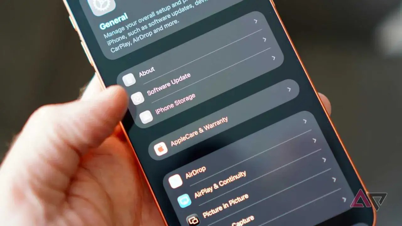 Dłoń trzyma iPhone'a, na ekranie widać menu Ustawienia, gdzie można dokonać aktualizacji telefonu.