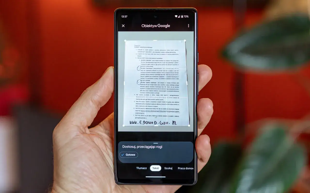 Smartfon skanuje dokument za pomocą Obiektywu Google. Widoczny jest interfejs aplikacji, który pomaga w dopasowaniu tekstu.